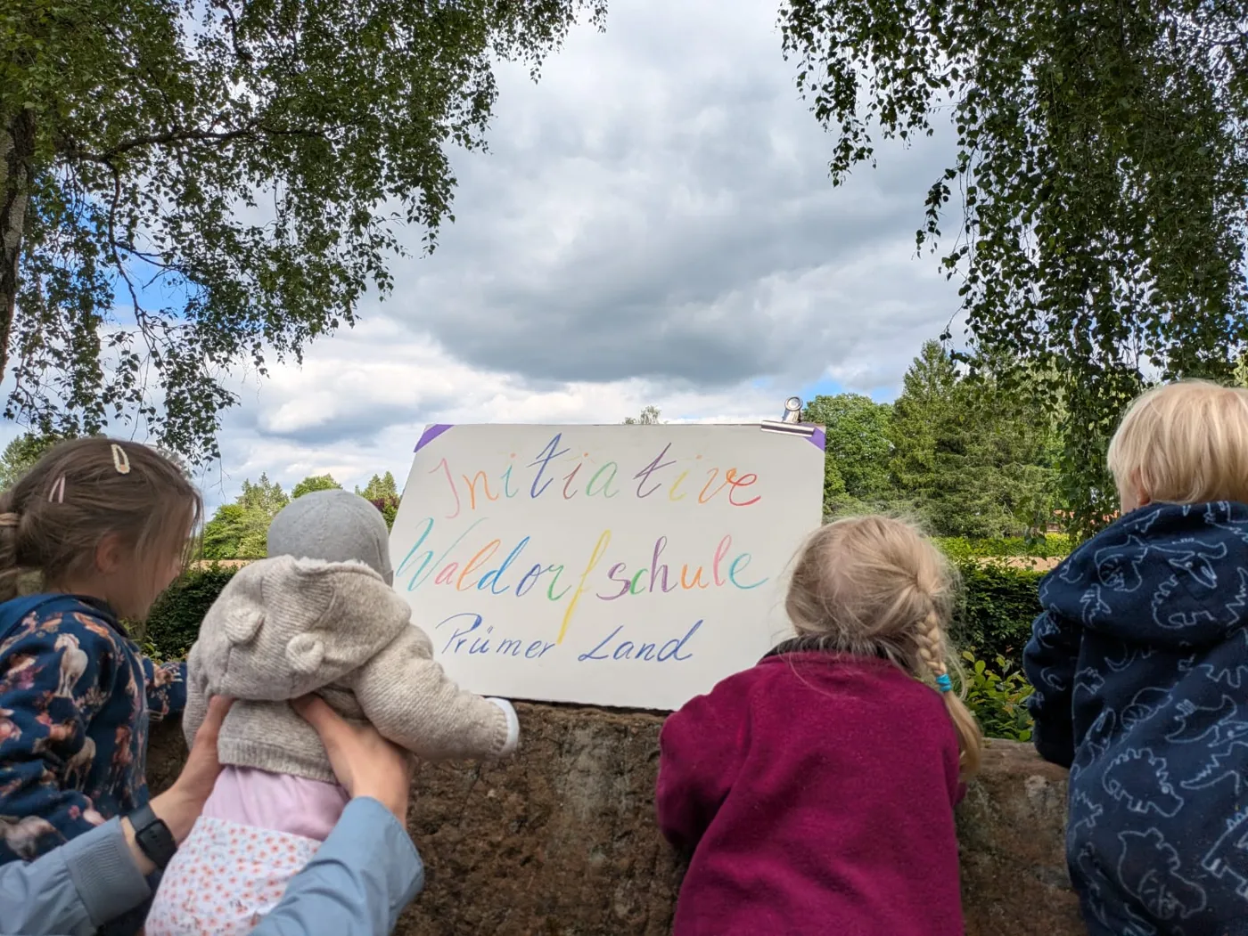 Kinder von hinten mit dem Schild der Initiative