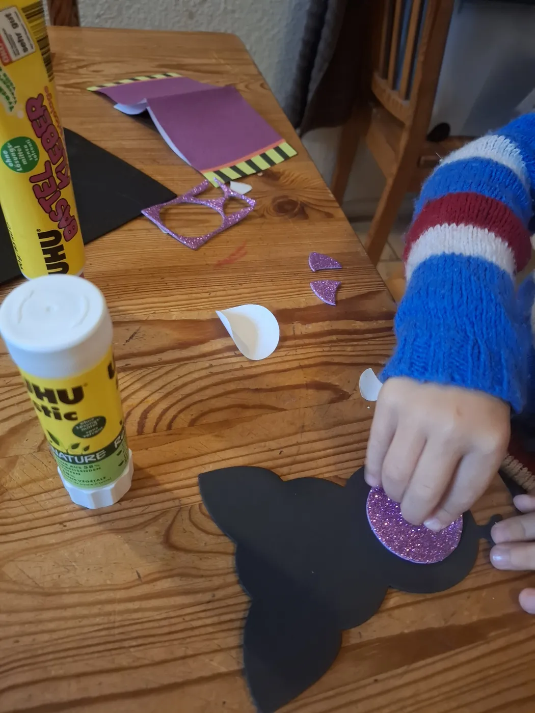 Kinderhände kleben eine Bastelarbeit aus Glitzerpapier